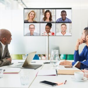 Gruppe bei hybrider Besprechung – Videokonferenz mit mehreren Teilnehmenden auf großem Bildschirm