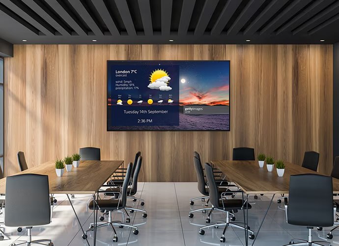 Ein moderner Konferenzraum mit einem großen Sony BRAVIA BZ35L 4K-Display an der Stirnwand, auf dem Wetterinformationen und Präsentationsinhalte für eine bevorstehende Besprechung angezeigt werden.